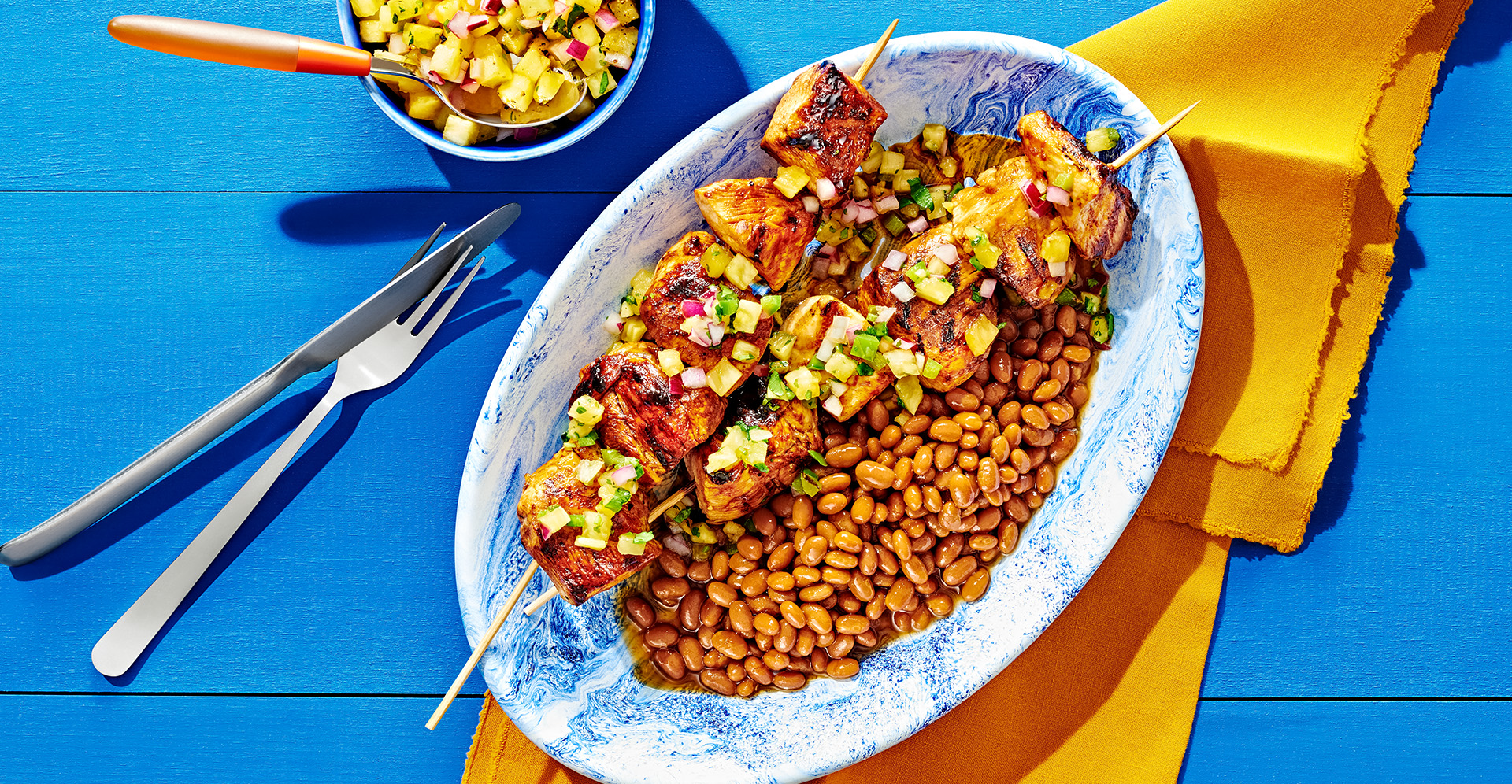 Grilled chicken skewers and baked beans on an oval blue and white swirl pattern plate