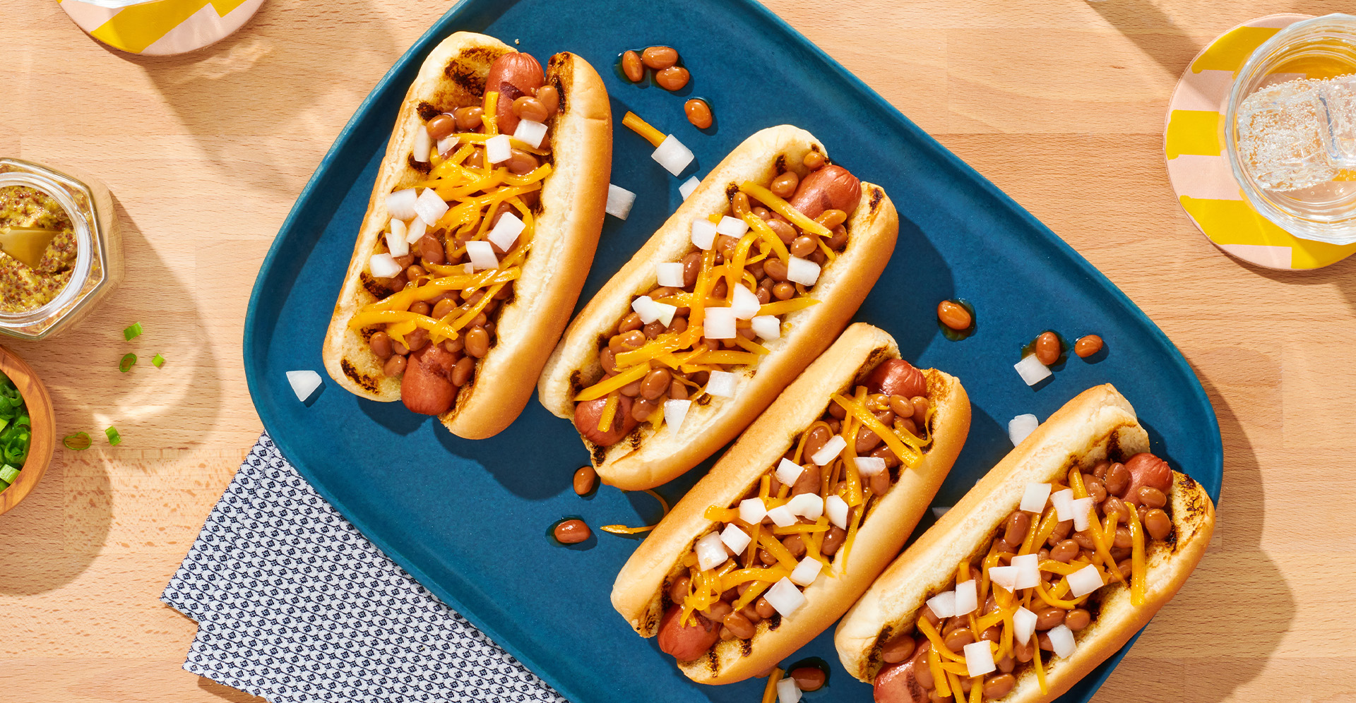 Four hot dogs with cheese, baked beans and onions on blue platter