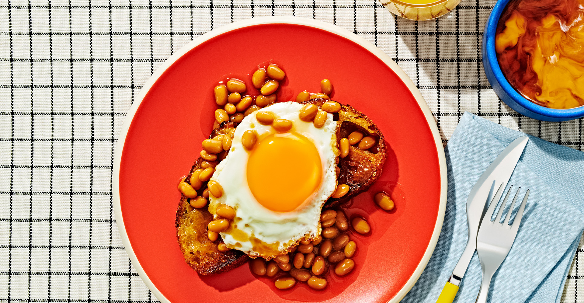 Sunny side up egg on a piece of toast covered in baked beans on a red plate