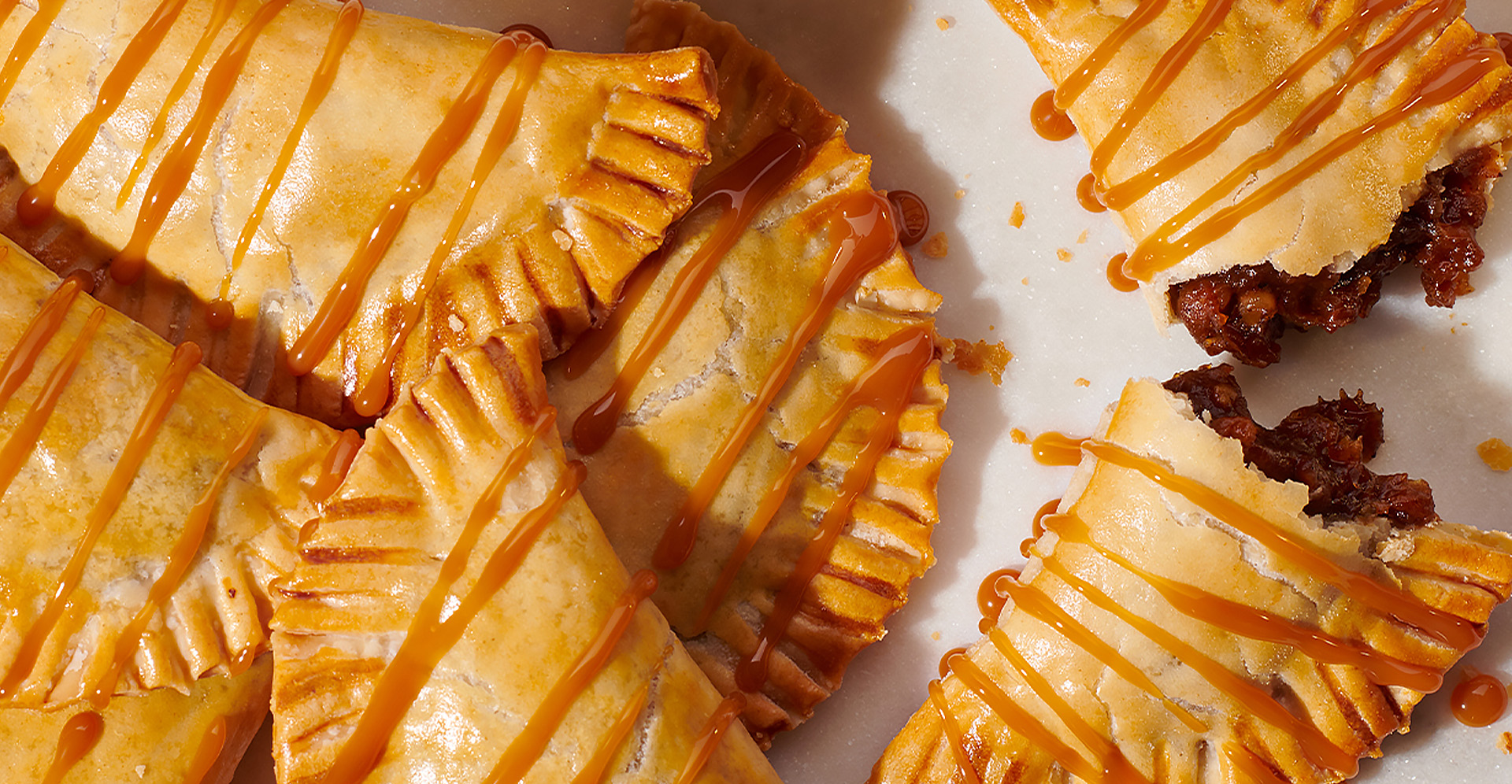Close-up of bourbon and brown sugar pumpkin empanadas, one split in half to reveal filling on white plate.