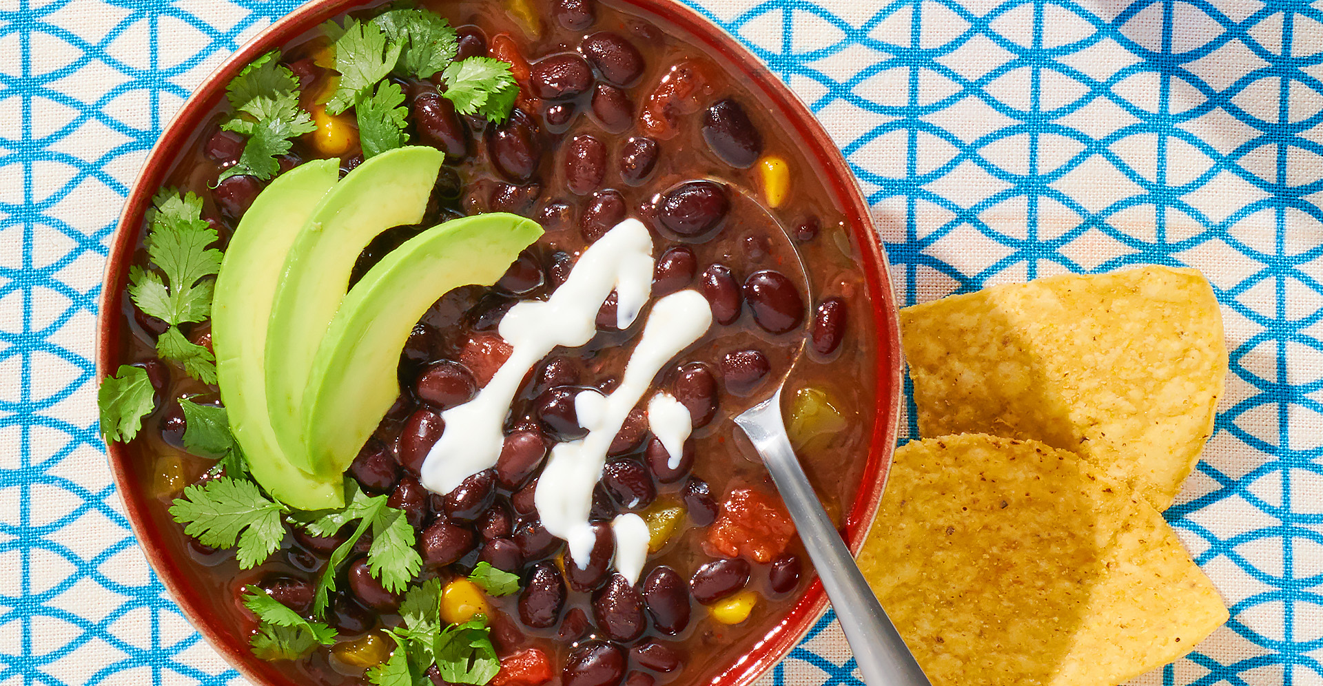 Bowl of black bean soup garnished with cilantro, sour cream and avocado