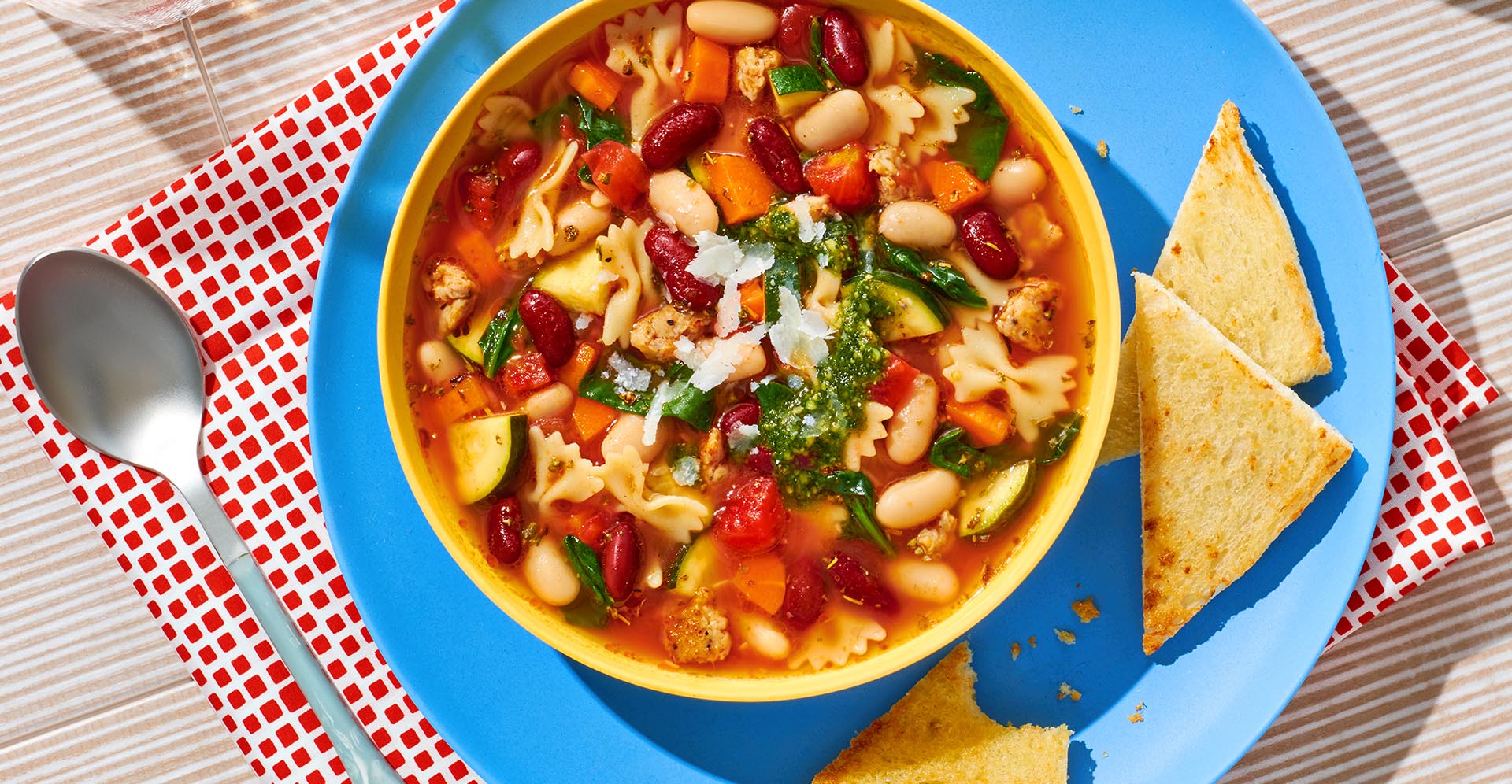 A bowl of red and white bean minestrone soup with bowtie pasta on a blue plate