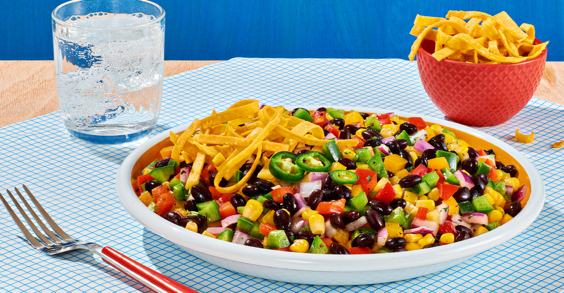 Black bean and corn salsa on a white plate with tortilla strips and a glass of sparkling water