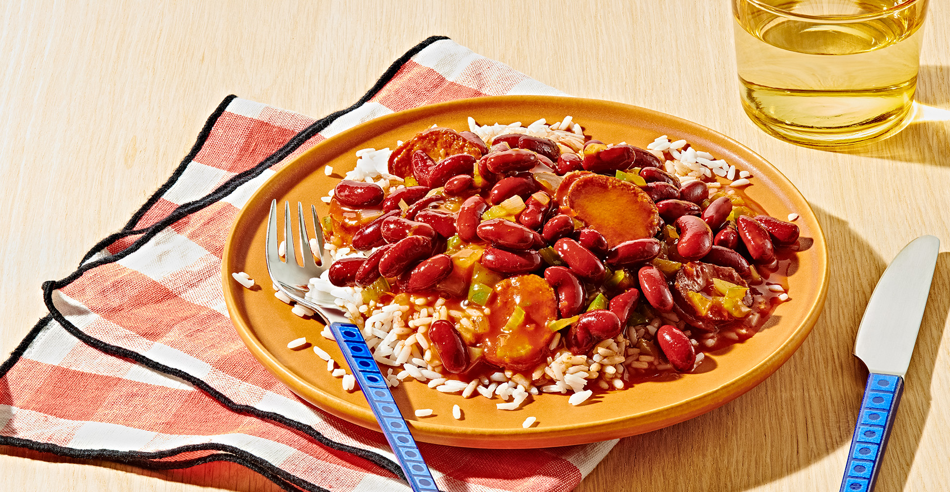 Red beans and rice with vegetables on a mustard colored plate with fork, knife, and a glass of water