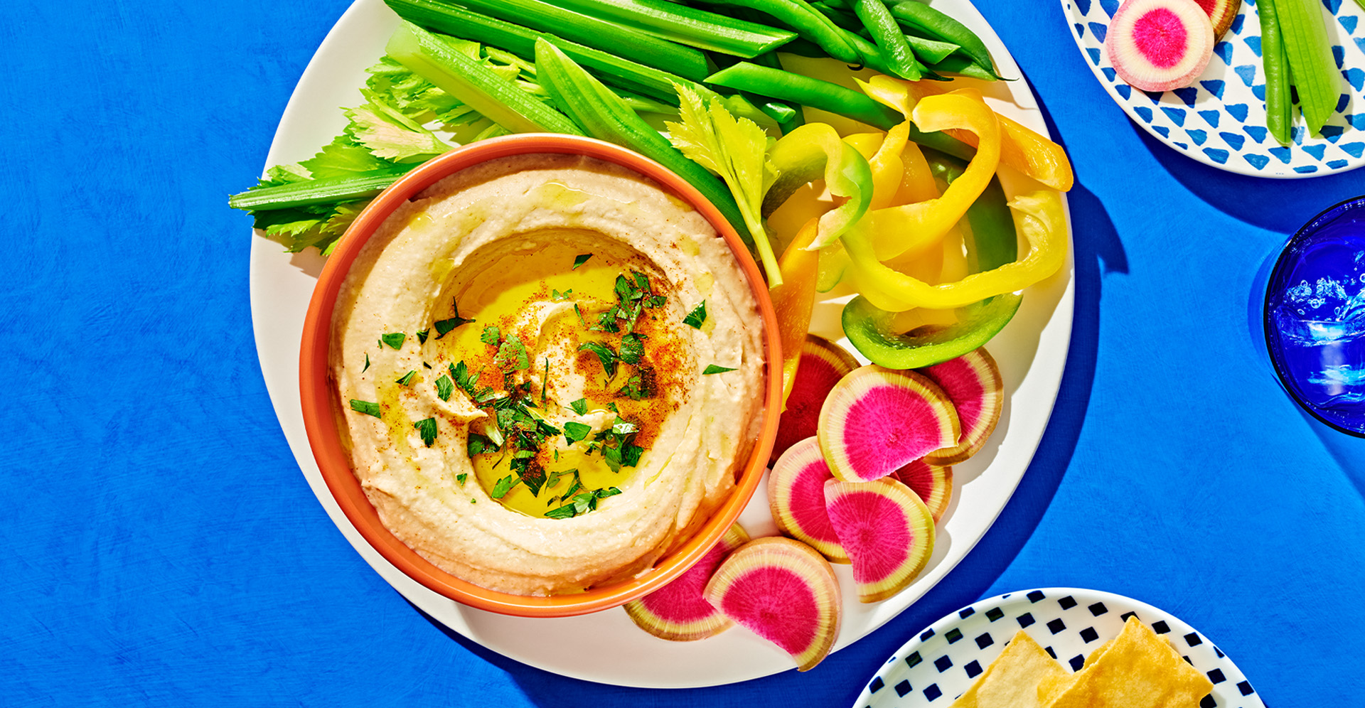 Close-up of hummus with olive oil and fresh herbs in an orange bowl