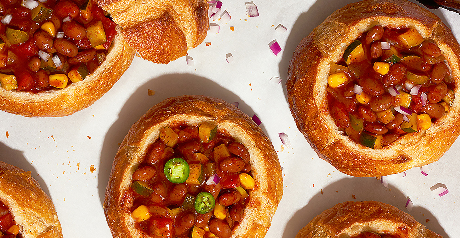 Five bread bowls on a baking sheet filled with vegetarian chili
