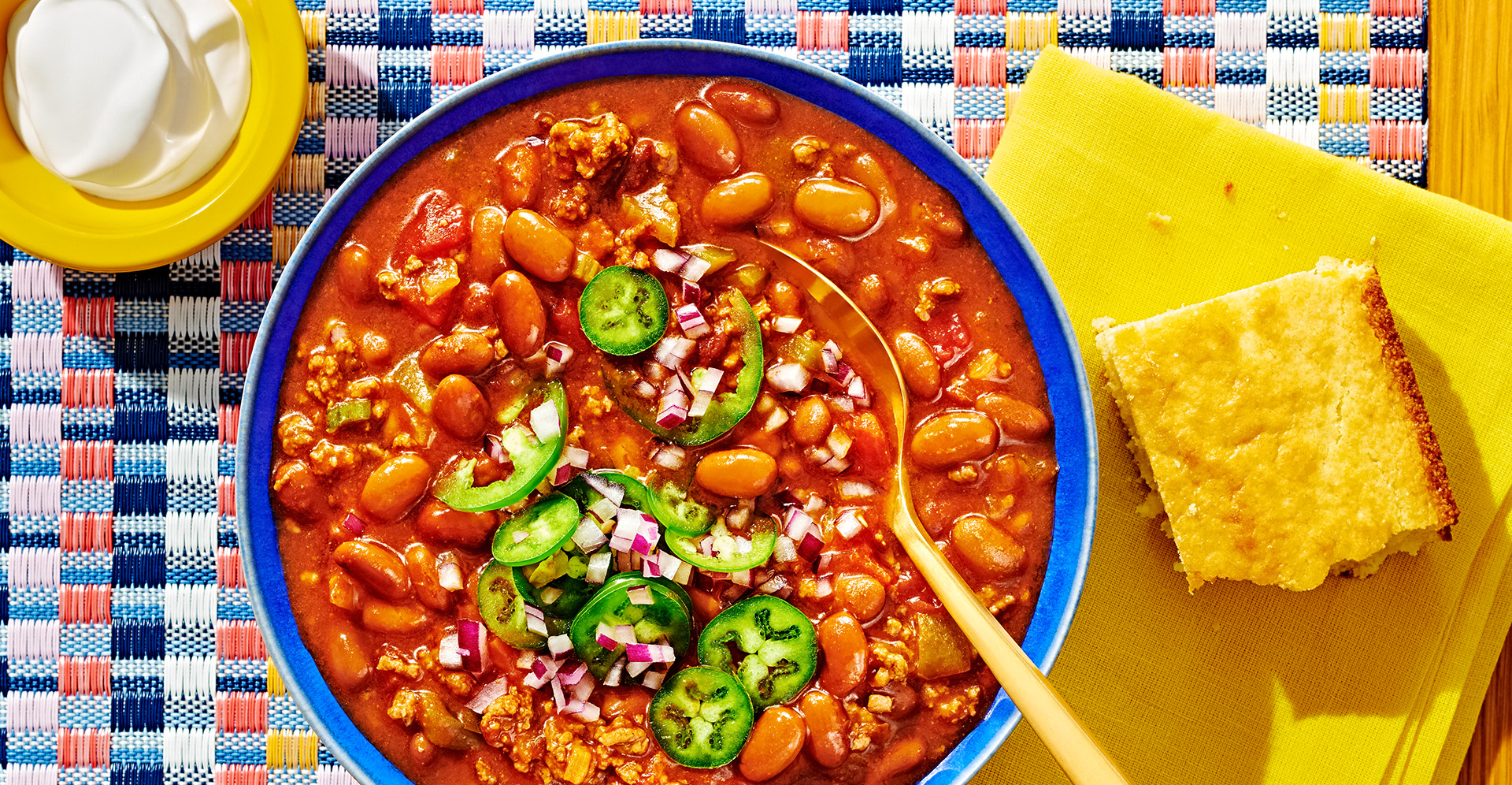 Bowl of chili and spoon in blue bowl garnished with jalapenos and a side of cornbread