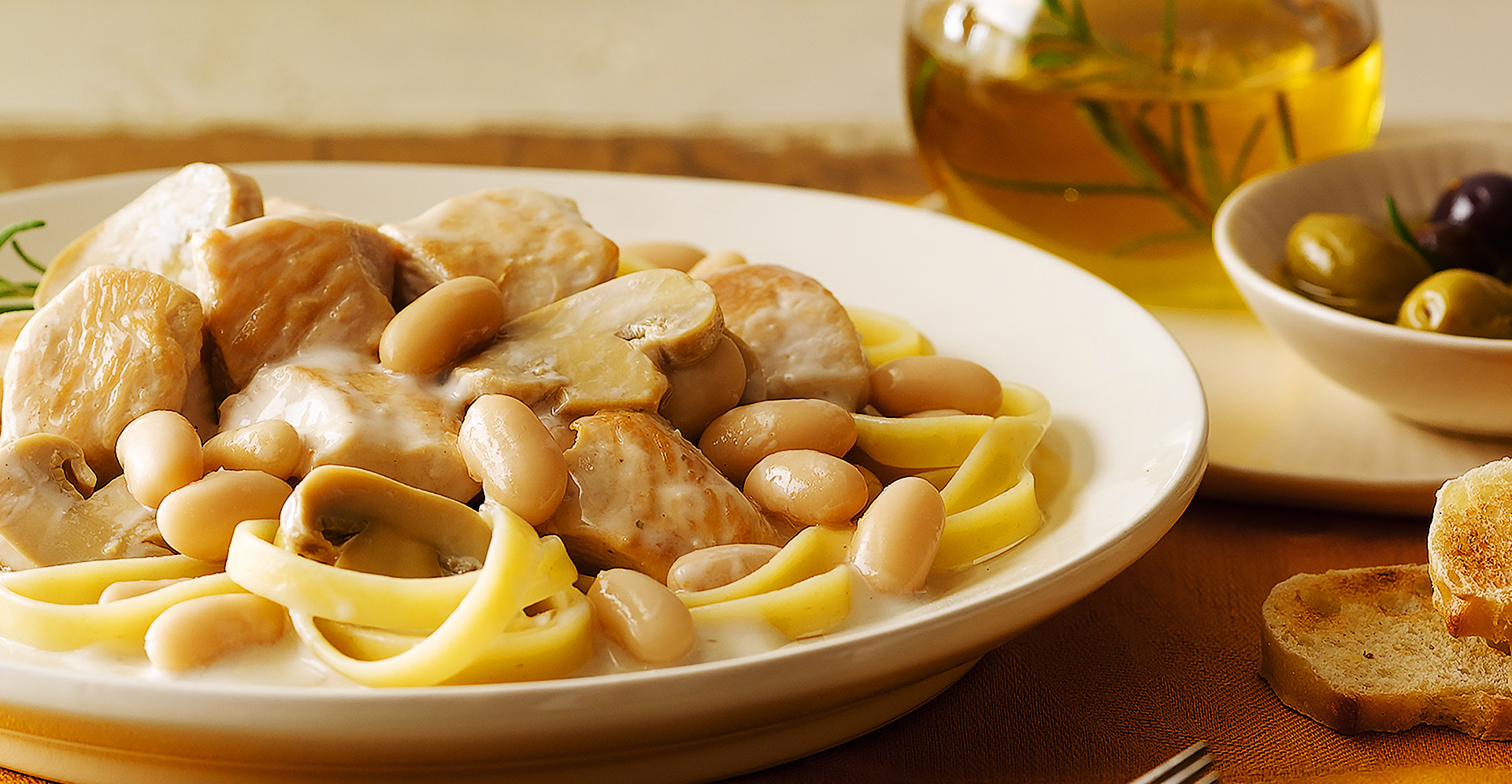 Creamy Tuscan Chicken and Mushrooms with cannellini beans over past on white plate