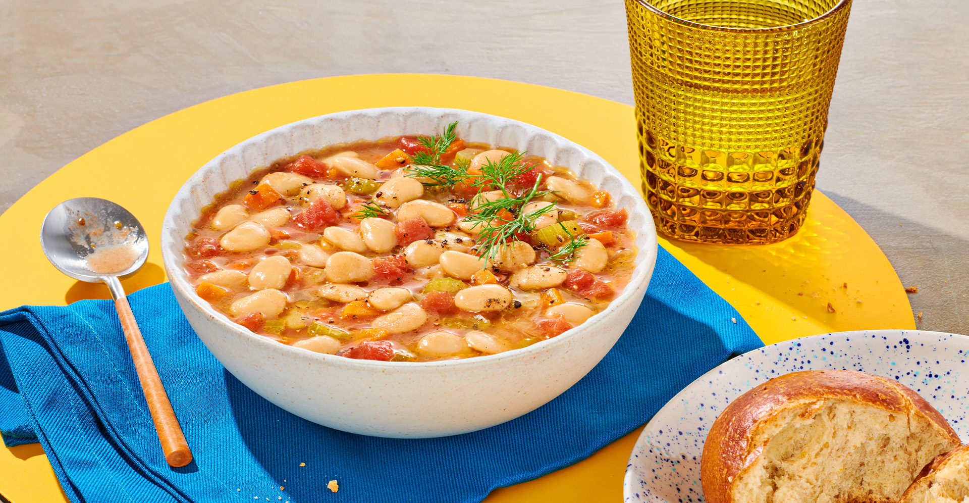 Butter bean soup in a white bowl with silver spoon on blue placemat