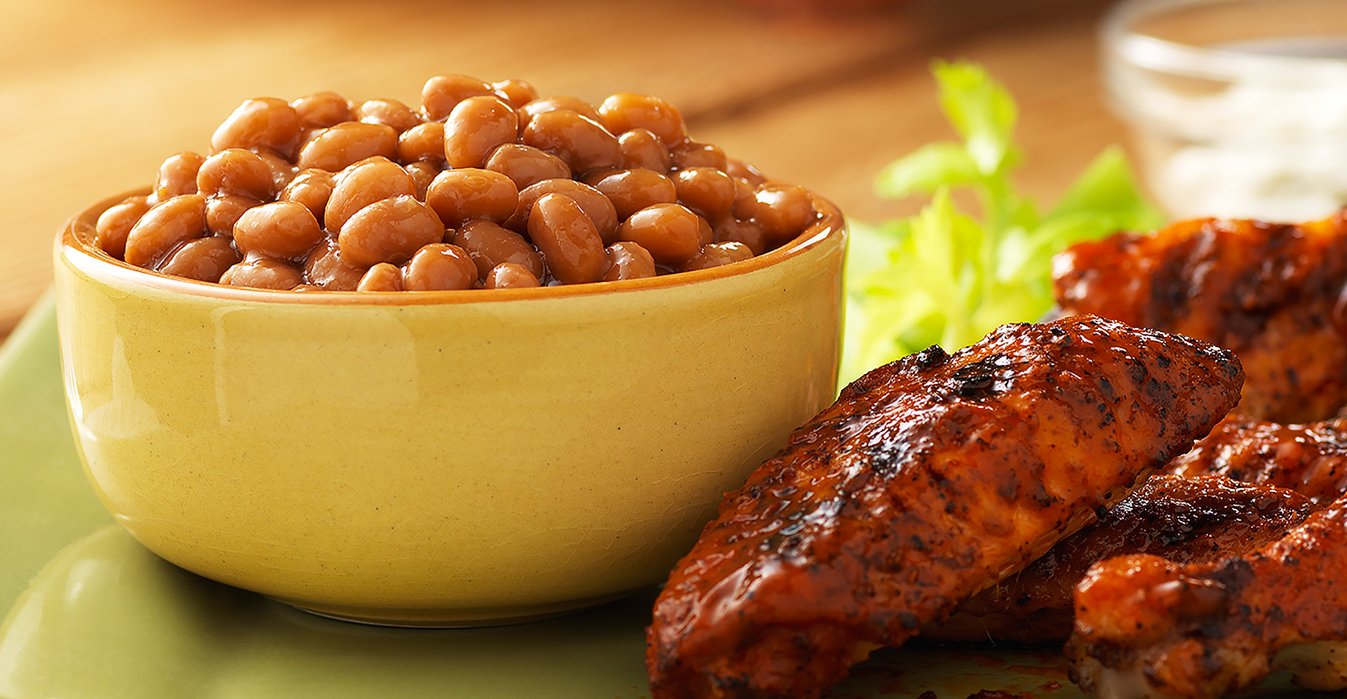 Grilled buffalo wings next to a yellow bowl of baked beans