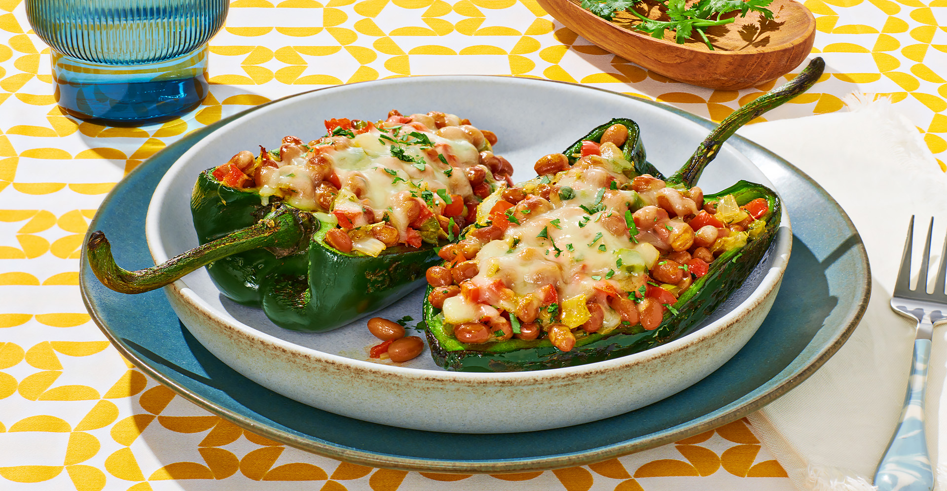 Grilled green chili rellenos with baked beans, tomatos, onions and cheese in light blue bowl with side of cilantro