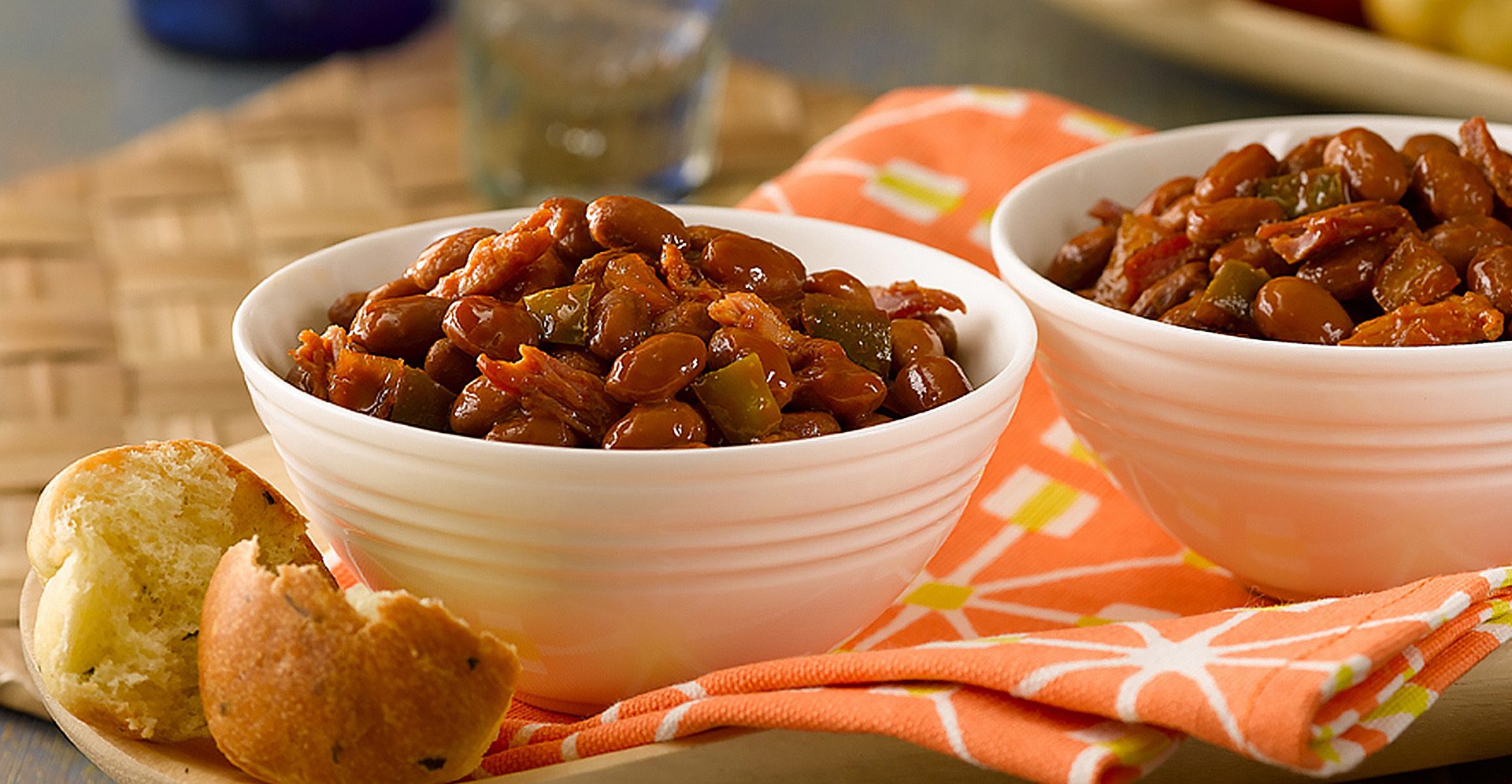 Carribbean spicy pork and red beans in two white bowls with a bread bun