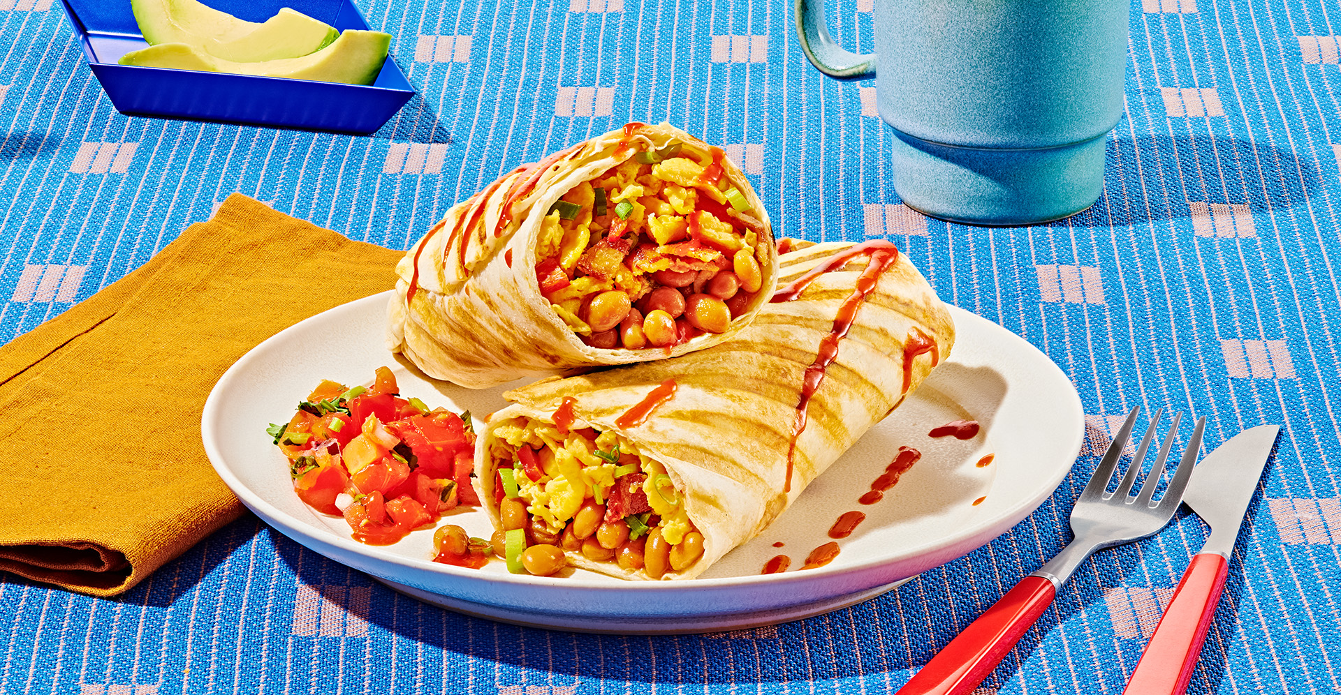 Grilled egg and baked bean breakfast burritos with bacon and tomato salsa on a white plate on a blue tablecoth
