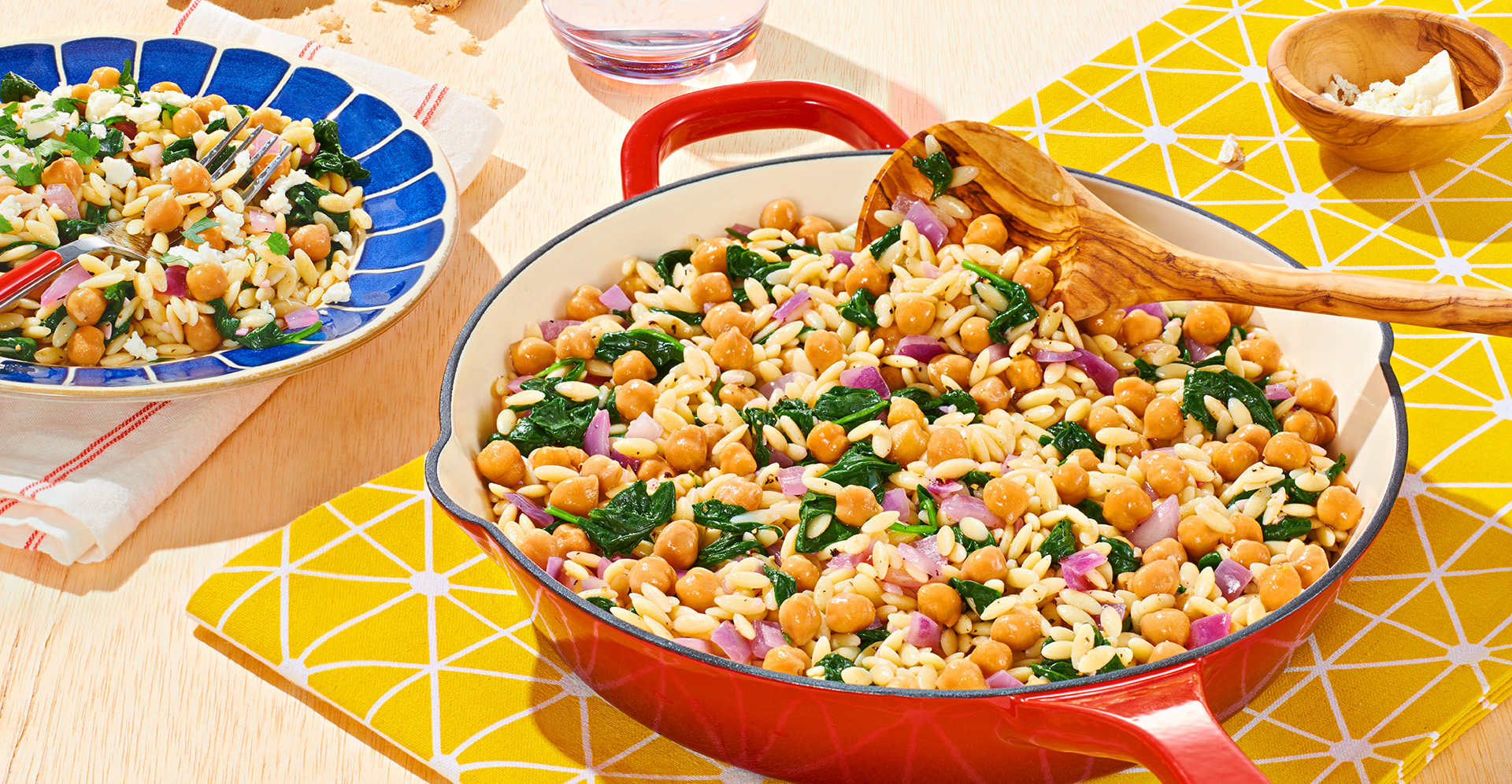 White enamel skillet filled with orzo, spinach and garbanzo beans, also known as chickpeas