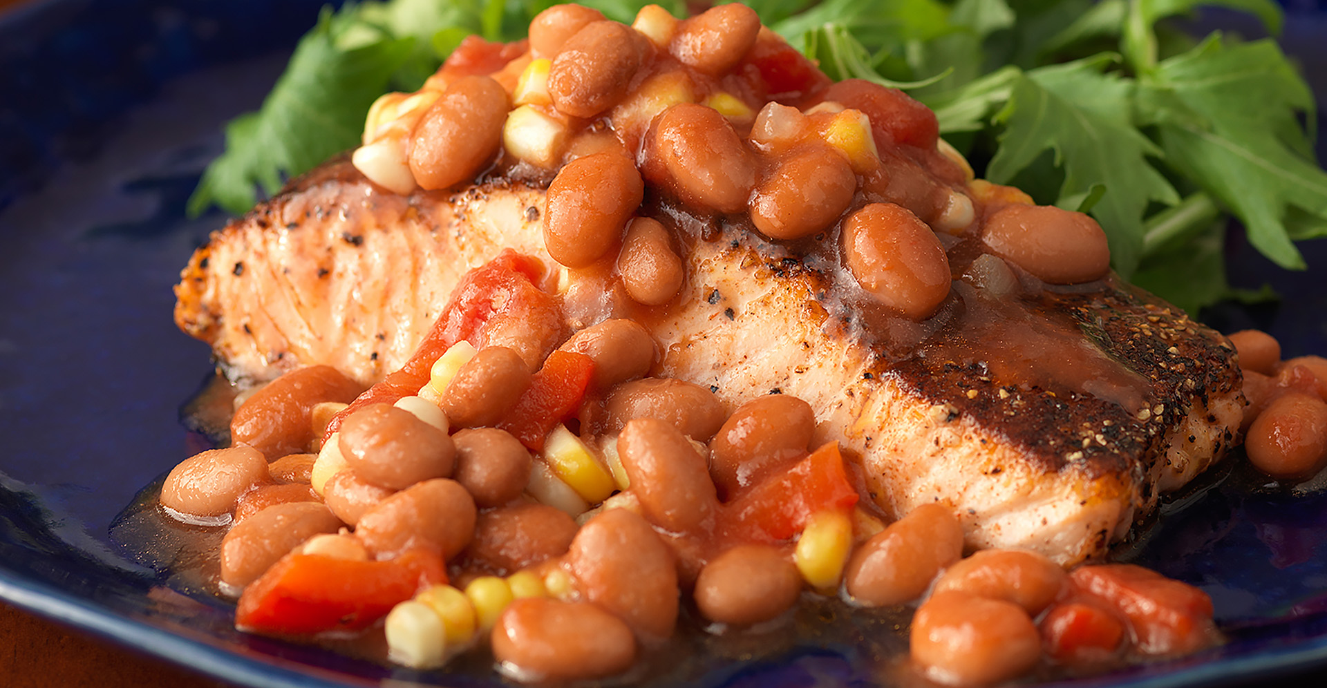 Pepper crusted salmon with pinto beans and greens on blue plate