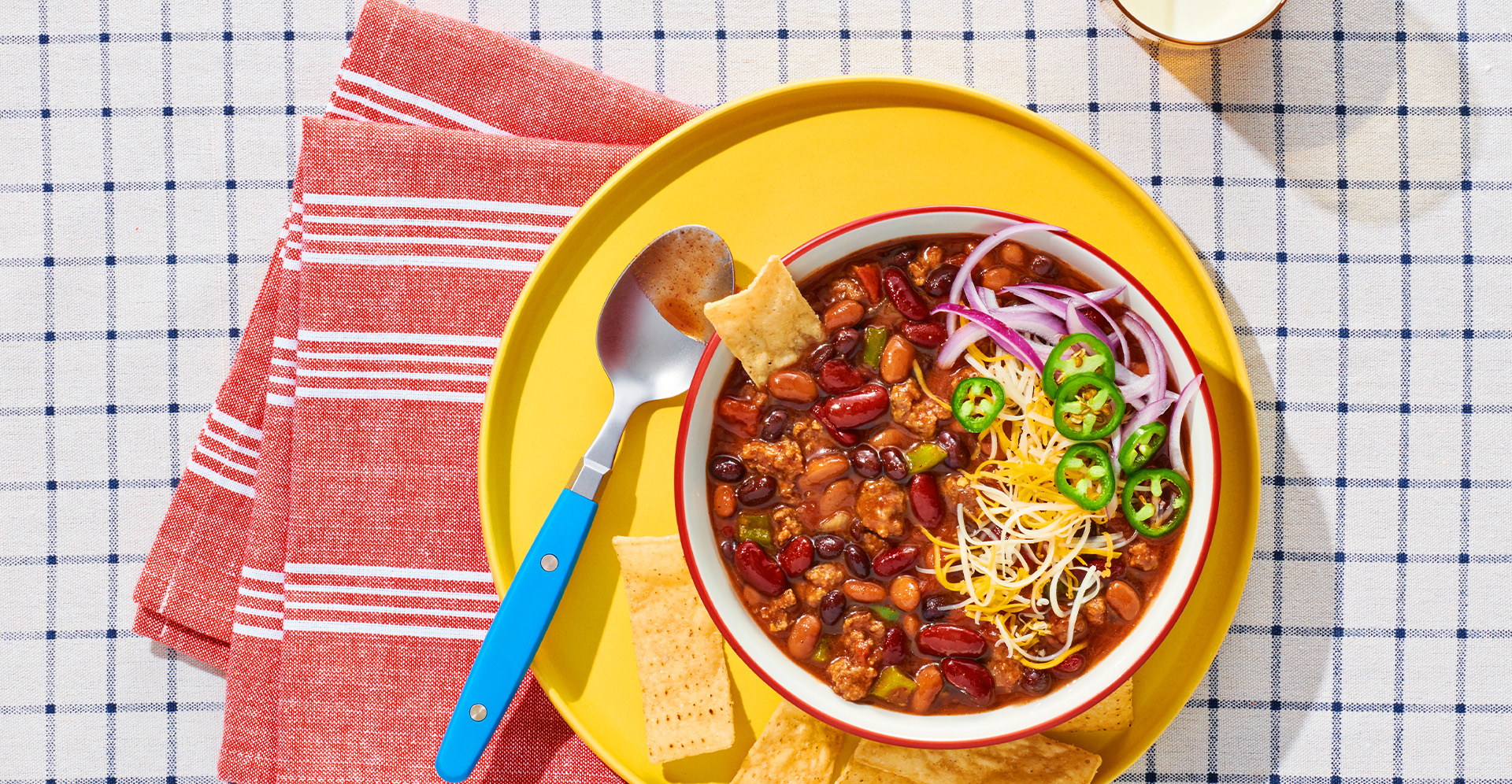 Chili with jalapenos, cheese and onions with tortilla chips on a yellow plate