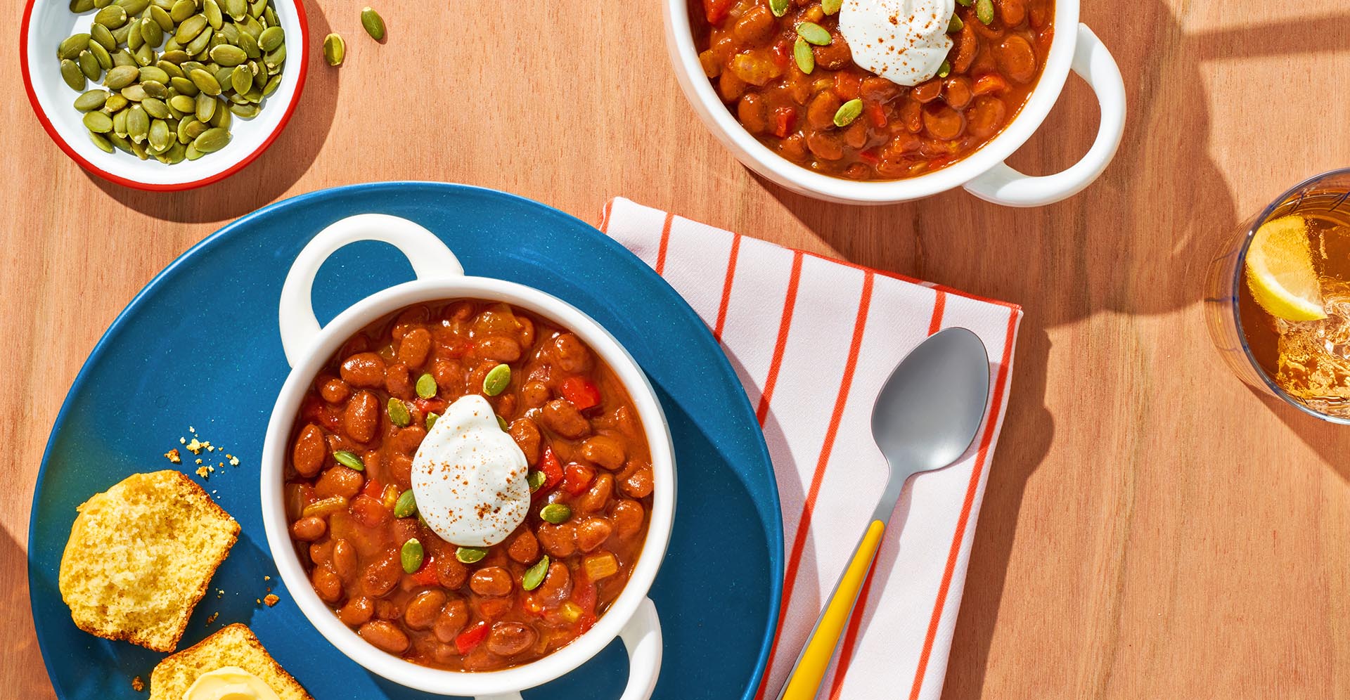 Two bowls of pumpkin chili on a table with a side of cornbread and pepitas