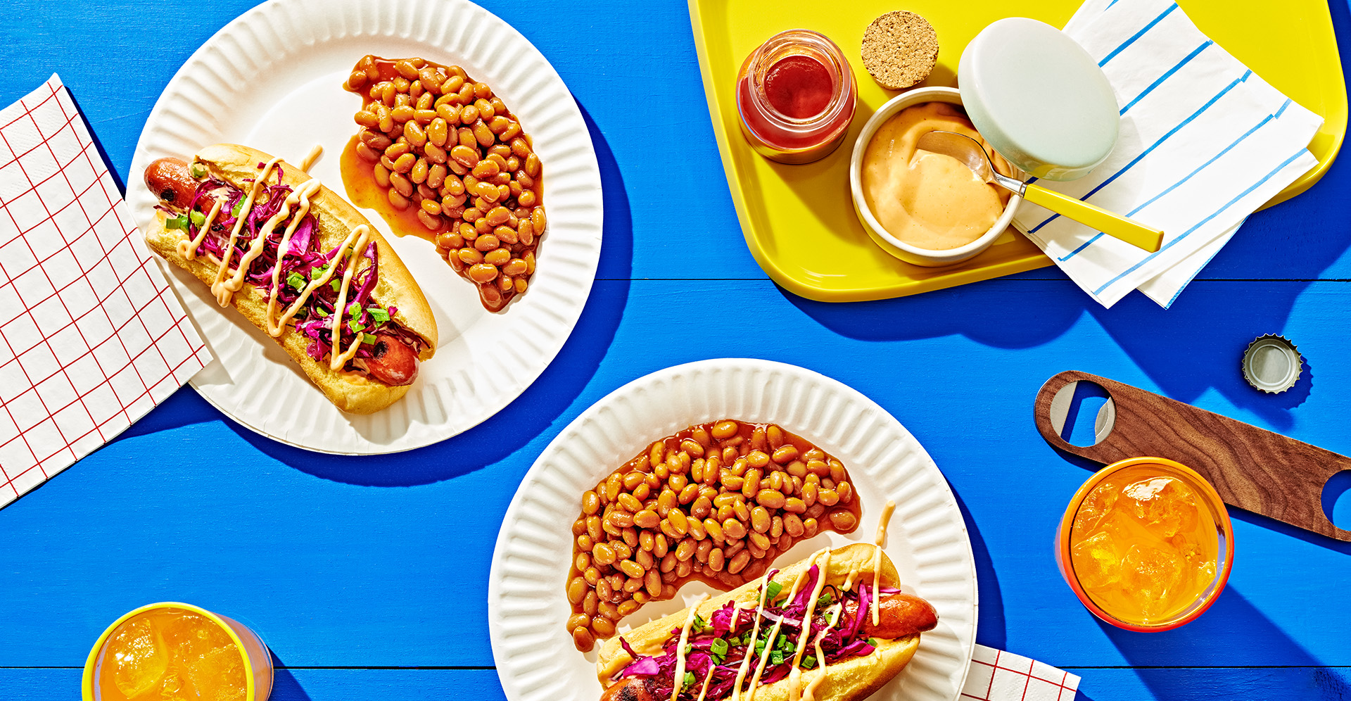 A hot dog with Asian slaw and mustard and side of baked beans on a white paper plate