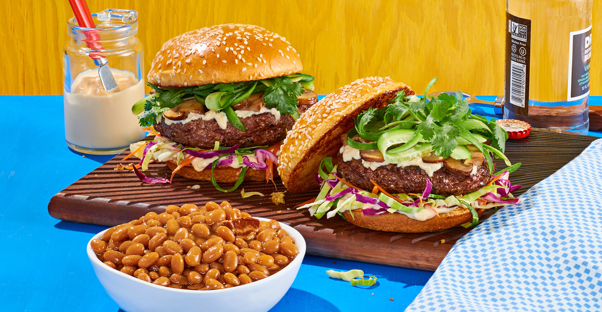 Two bison burgers with lettuce, mayo and pickles with a bowl of baked beans with bacon