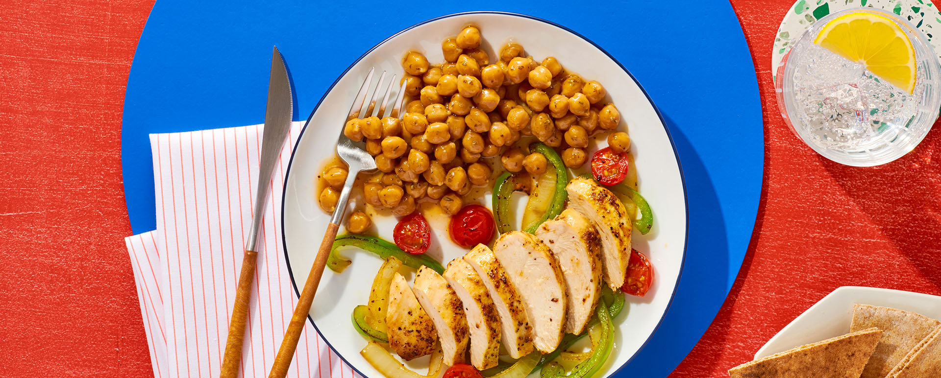 a white plate with sliced chicken and a serving of chickpeas sitting on a blue placemat.