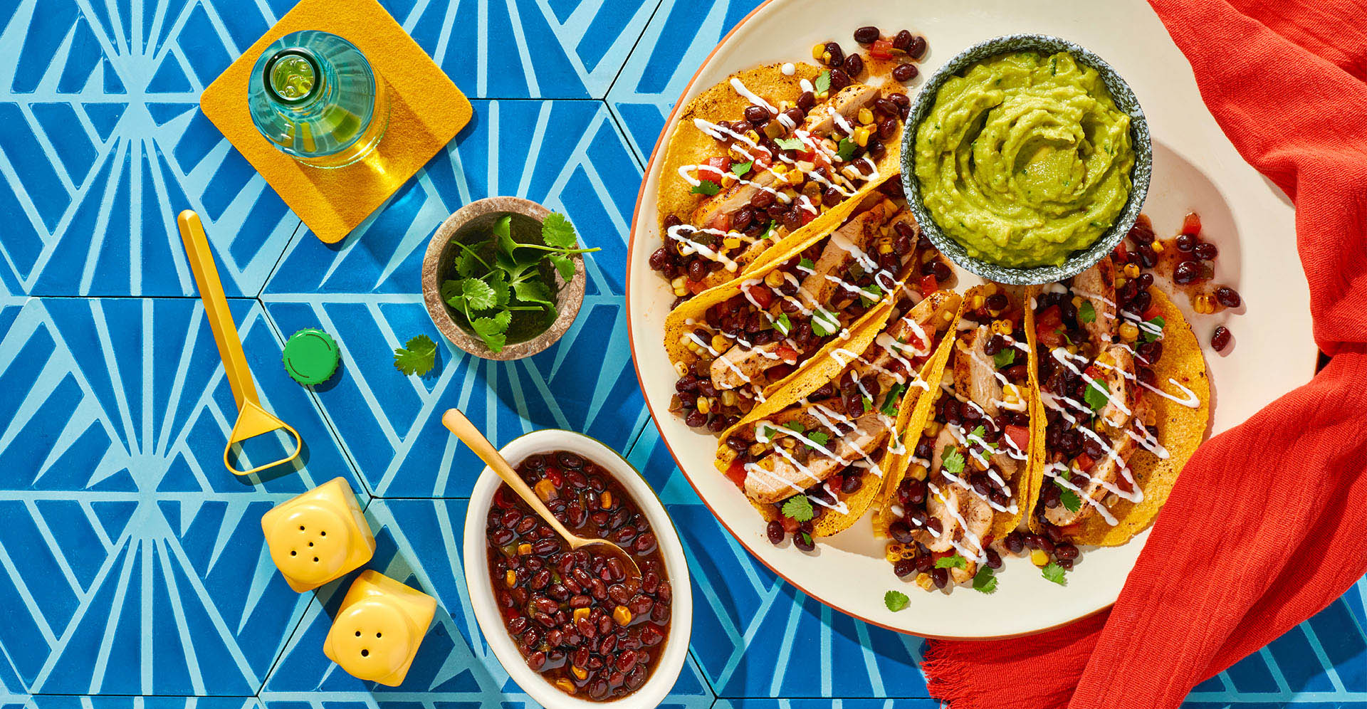 chicken tacos plated with guacamole on a table with a side of beans