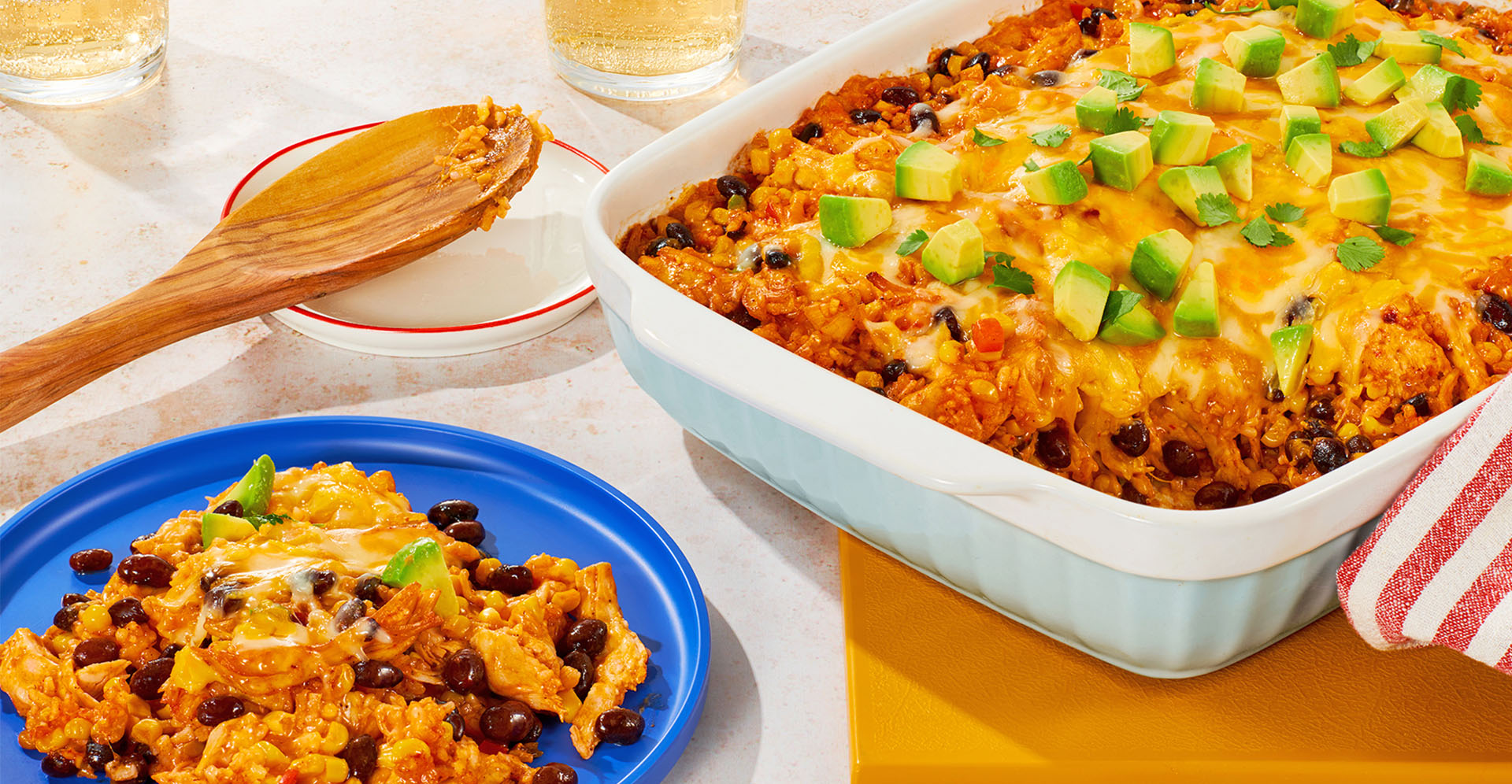 A casserole dish full of taco bake sitting next to a blue plate with a serving of the meal on it. 