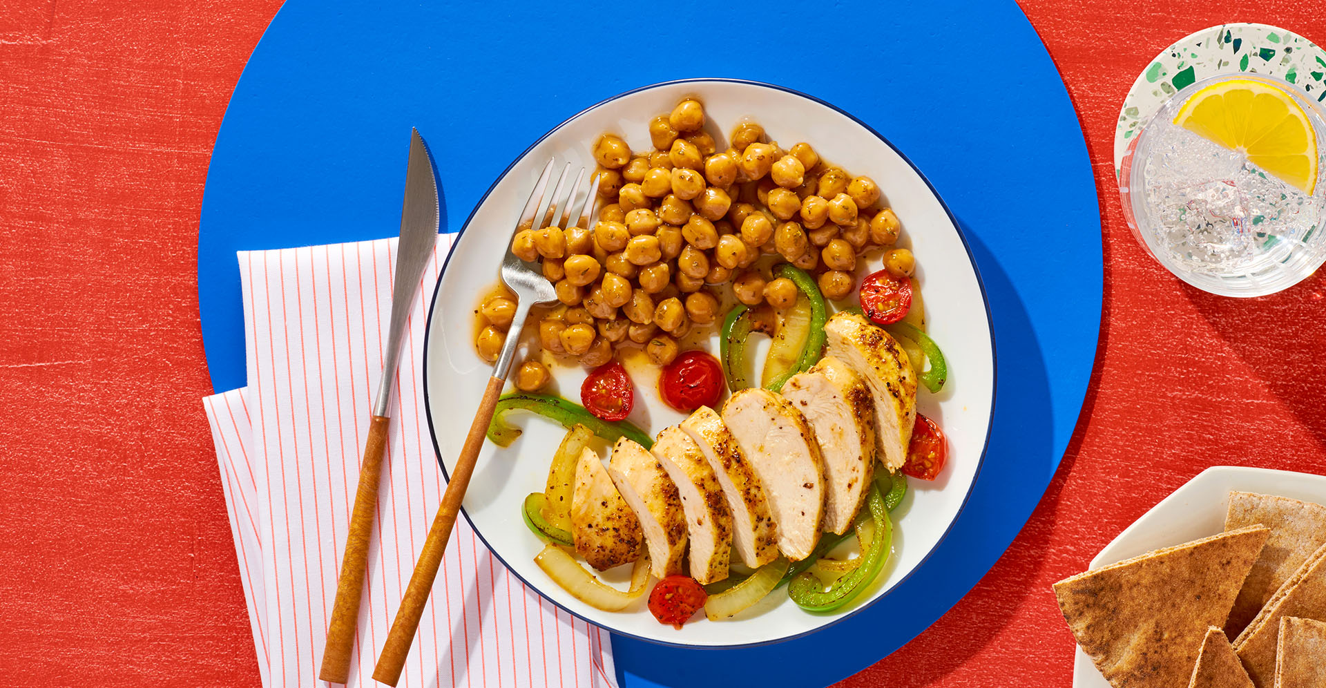 a white plate with sliced chicken and a serving of chickpeas sitting on a blue placemat.