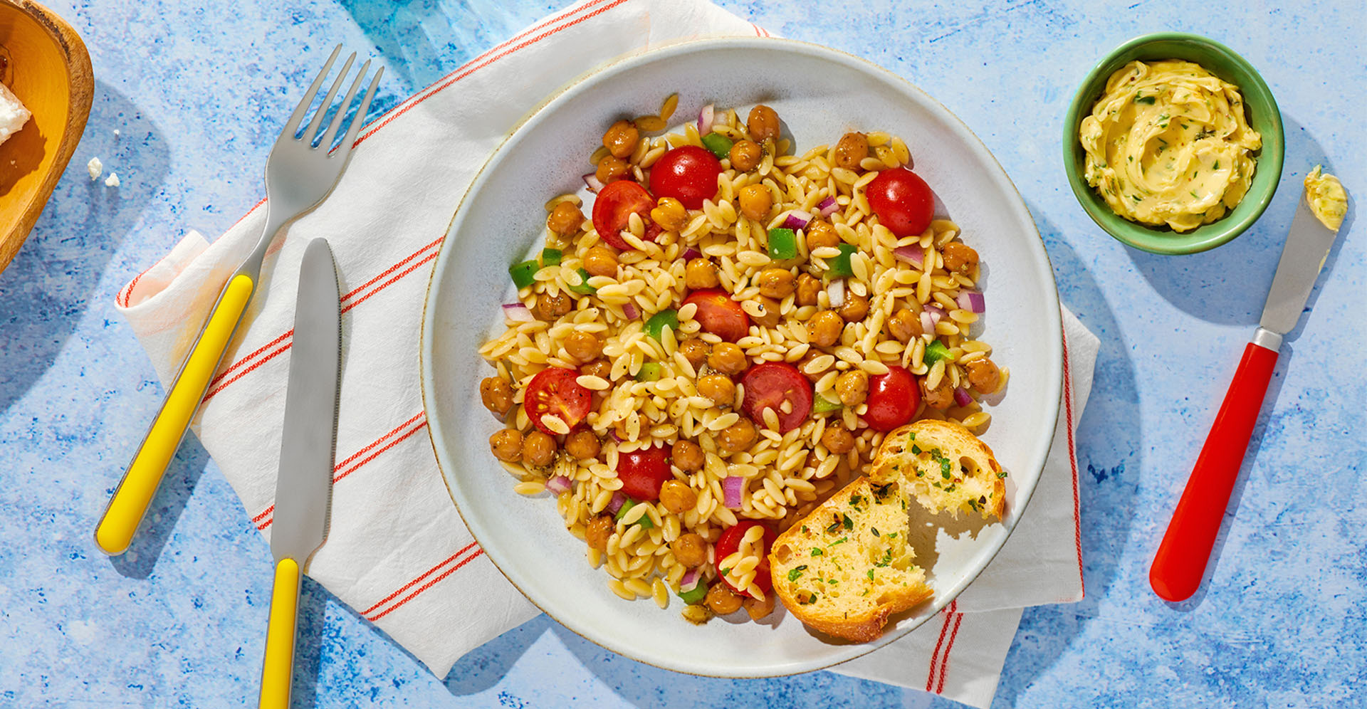 A white bowl filled with orzo salad sitting on a set blue table.