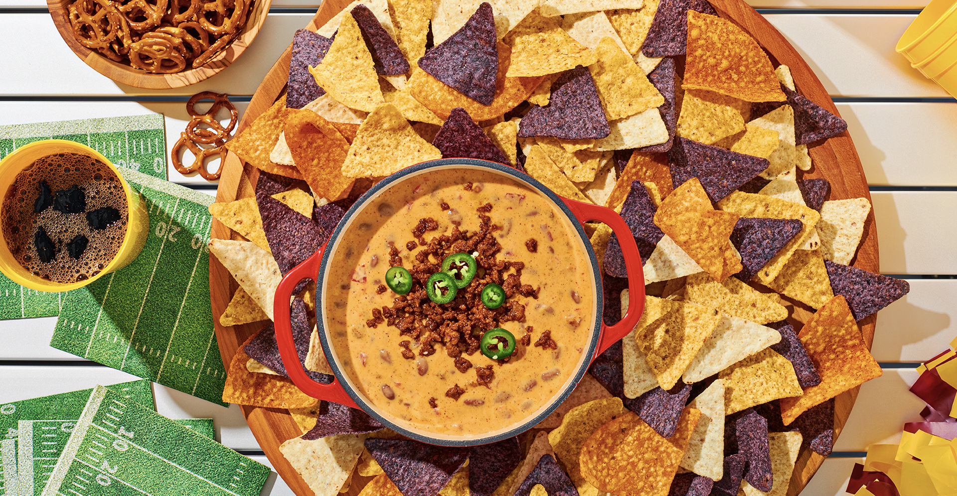 A Bowl of chili con queso in the middle of a plate of multi-colored tortilla chips.