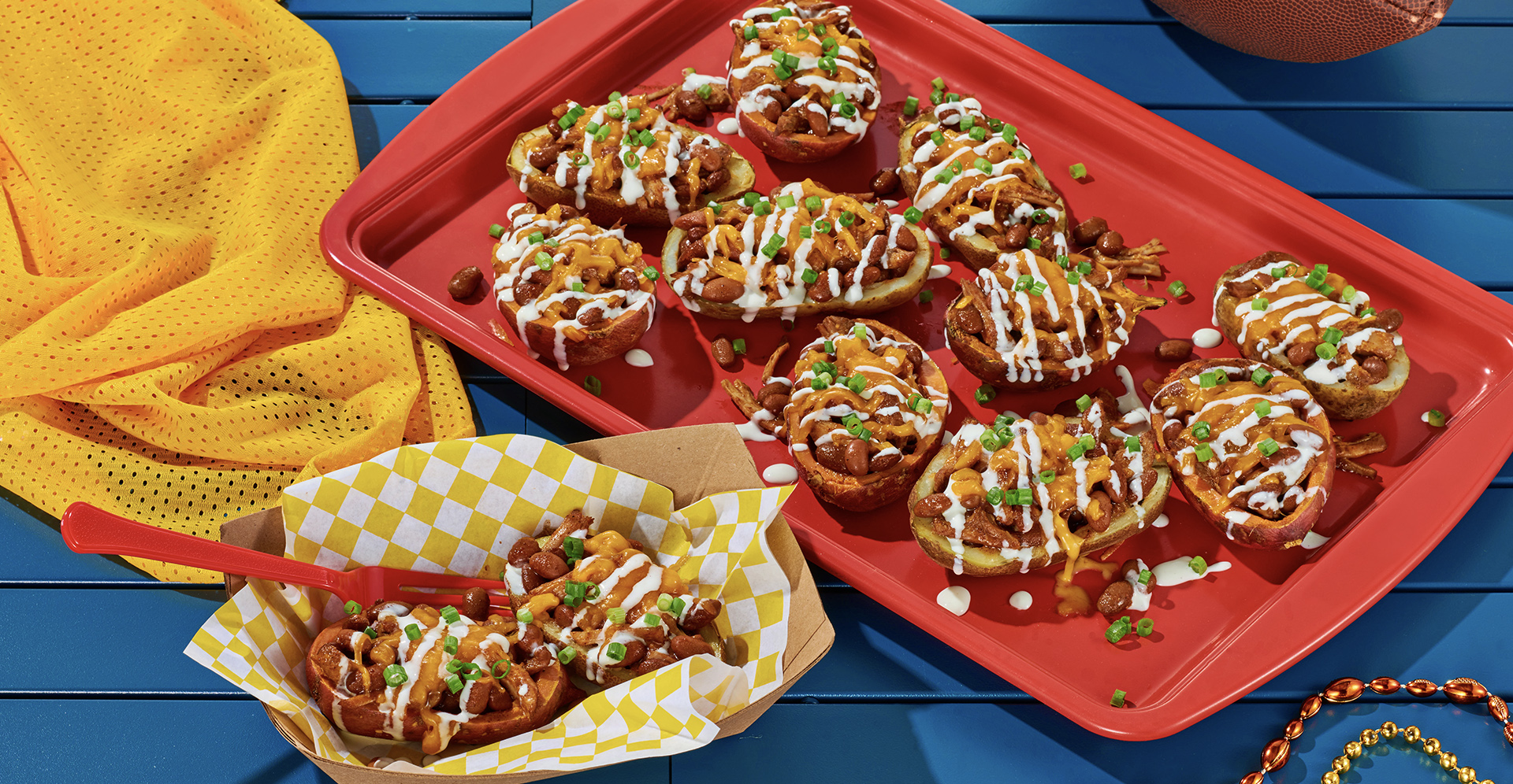 Loaded potato skins on a red tray sitting on a blue picnic table with a plate and a football nearby.