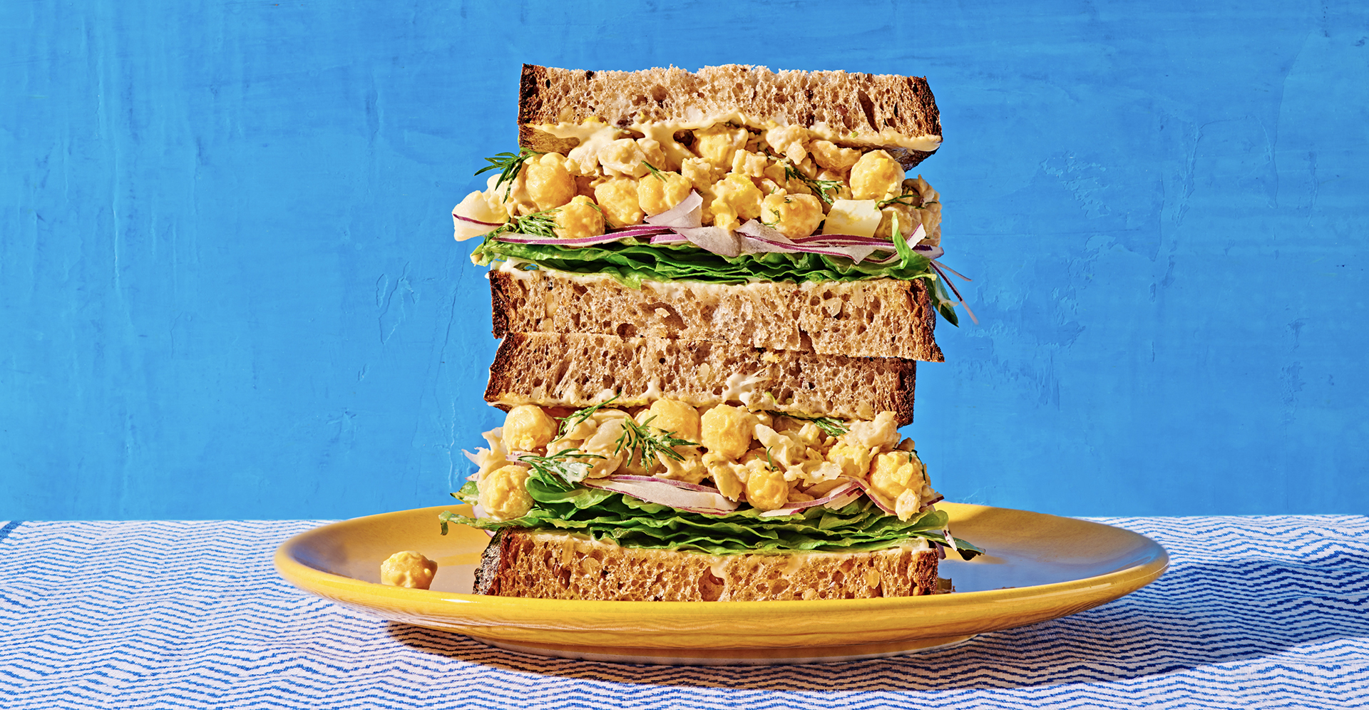 two halves of a sandwich filled with chickpea smash stacked on top of a yellow plate