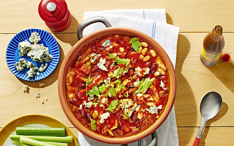 Buffalo chicken chili in orange bowl with celery, blue cheese, and Louisiana Hot Sauce