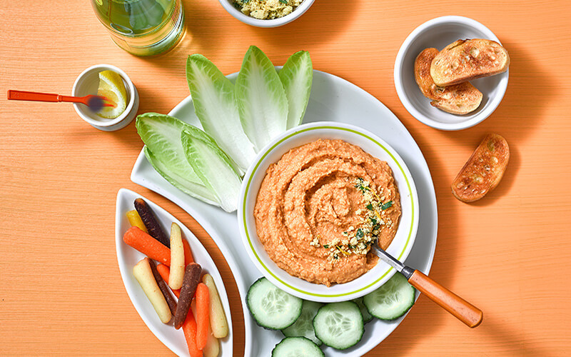 Rustic Tuscan Carrot Hummus in bowl surrounded by veggies