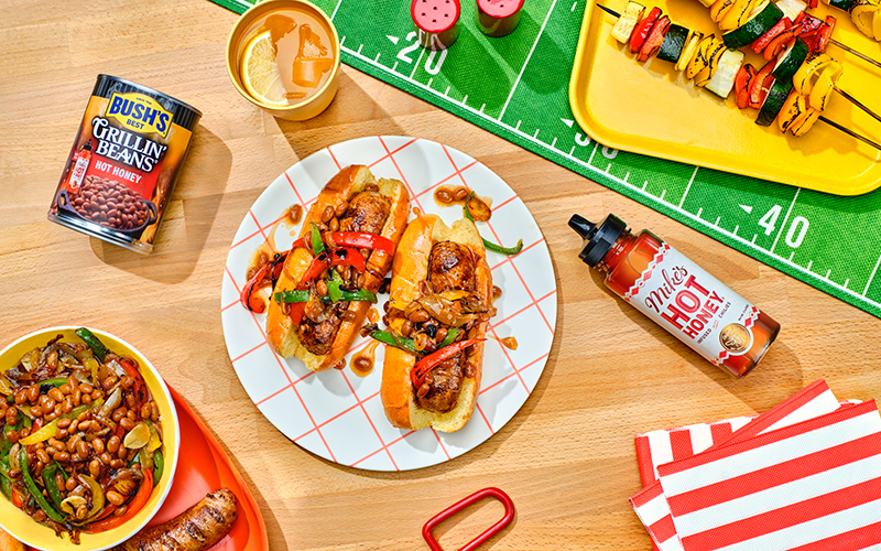 Italian sausages on buns covered in Bush's Hot Honey Grillin' Beans and drizzled with Mike's Hot Honey.