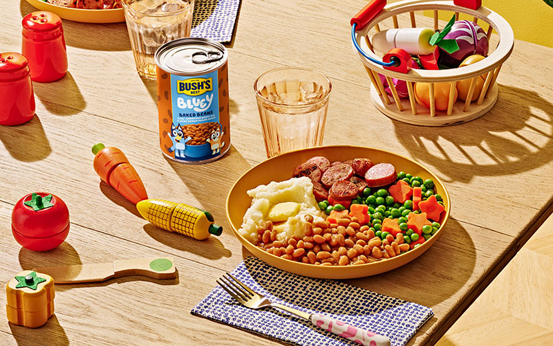 Plate with baked beans, mashed potatoes, sausages, and peas and carrots.