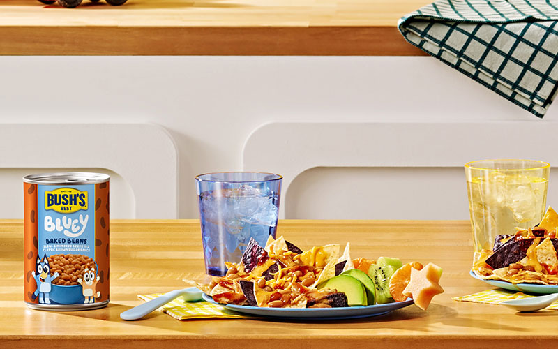 Plate of chicken nachos with avocado next to can of Bush's Bluey Baked Beans.