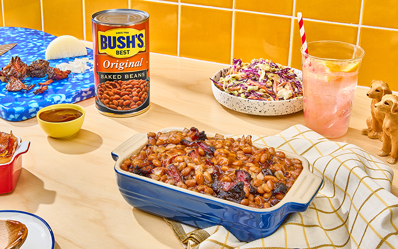 Bush's Baked Beans mixed with burnt ends and bacon in a blue baking dish