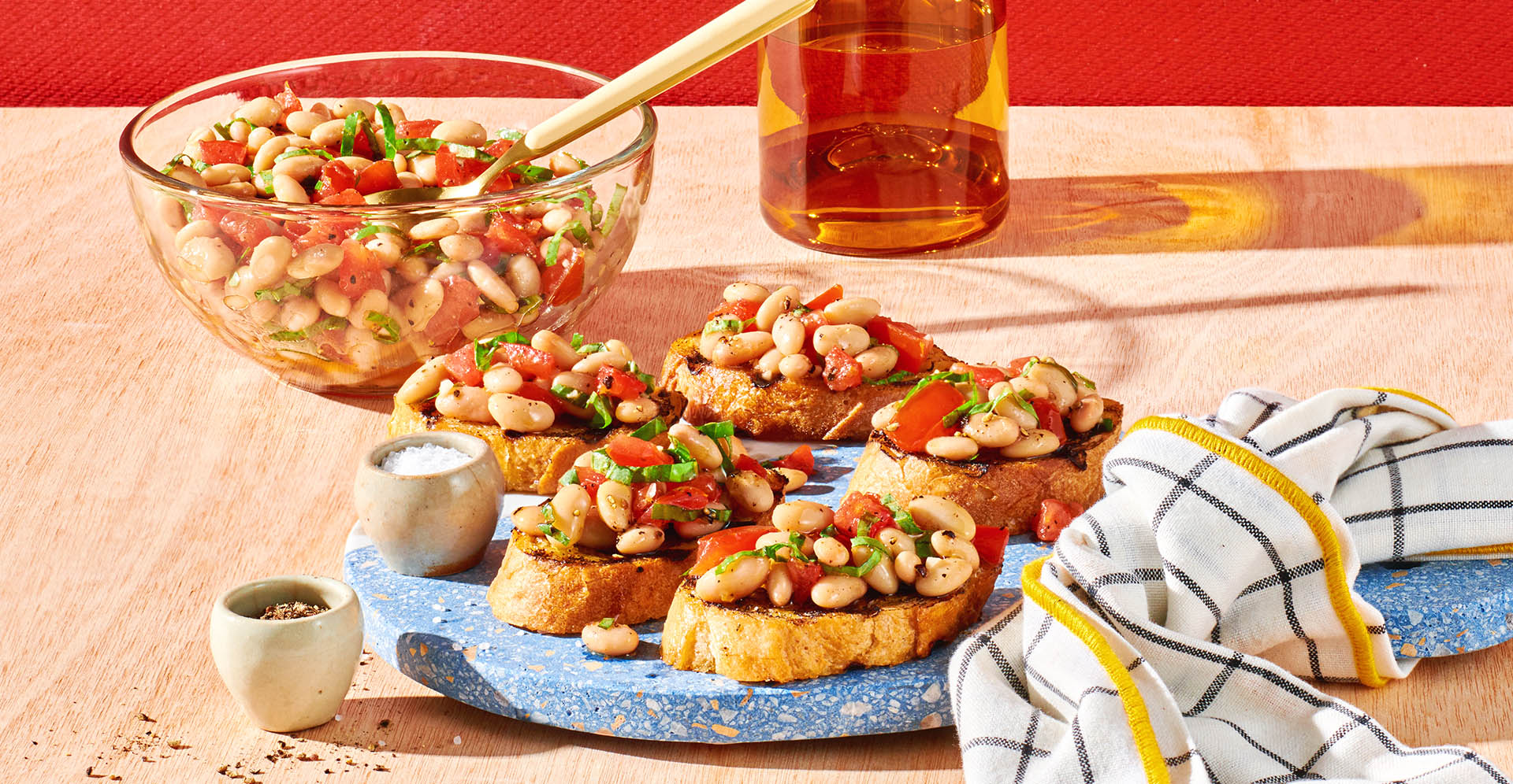 Plate of toasted bread topped bean, tomato and herb mixture, alongside bowl and napkin.
