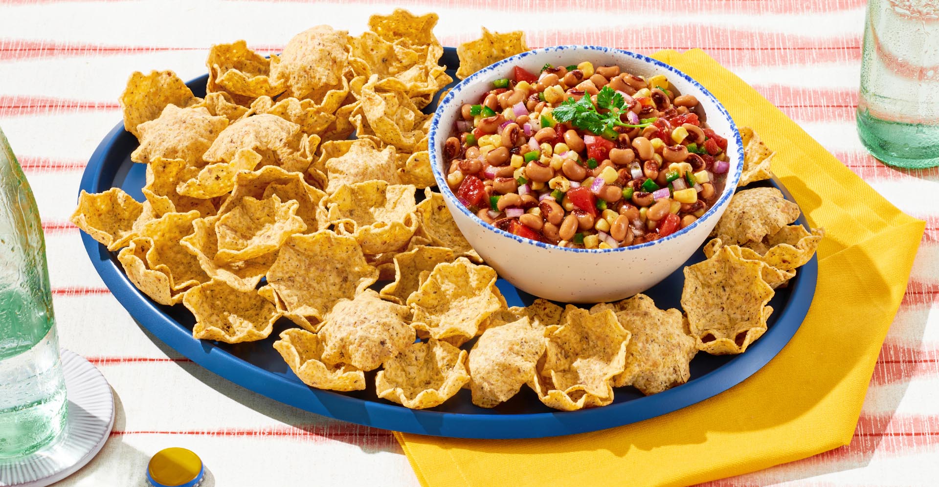 A bowl of black eye pea salsa on a blue plate of corn tortilla chips